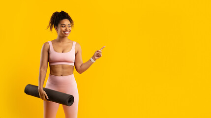 Smiling african american woman with yoga mat pointing