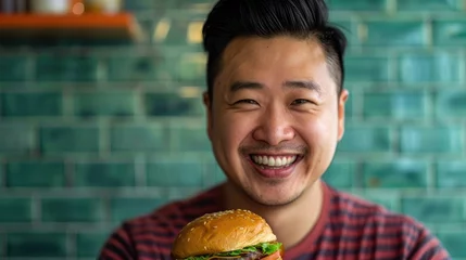 Fotobehang Happy Asian man smiling while holding a burger © 2rogan