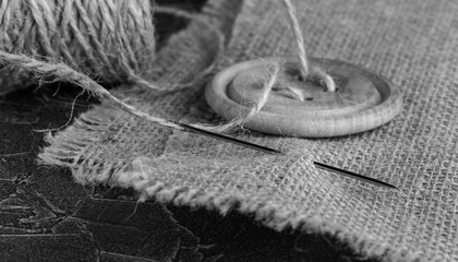 burlap, wooden button and sewing needle in black and white style close-up