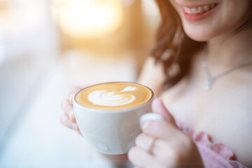 Close up holding Hot coffee latte with latte art milk foam in cup mug with happy Smiling woman...