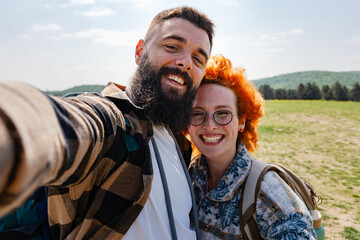 A beautiful and cheerful hiking couple captures a selfie with a stunning landscape in the background - 786656846