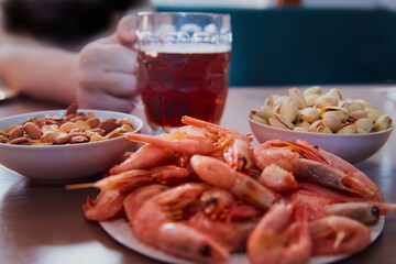 Hand taking a mug of beer on a table with nuts and shrimps, snacks in a beer bar, beer and snacks, snacks for beer in a beer bar, close-up
