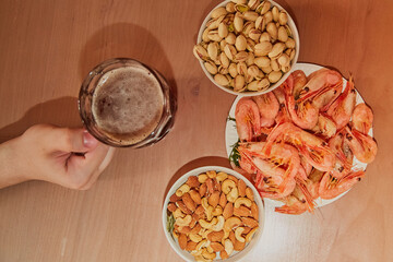 Hand taking a mug of beer on a table with nuts and shrimps, snacks in a beer bar, beer and snacks