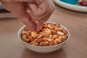 Hand taking almond nuts and cashews from a bowl on the table, snacks for beer, nut treats, nut allergy, close-up