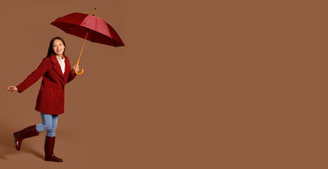 Beautiful young Asian woman with umbrella on brown background