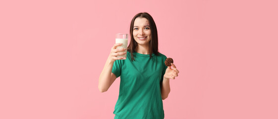 Beautiful young woman with tasty cookie and glass of milk on pink background