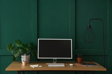 Stylish workplace with modern computer and houseplant near green wall