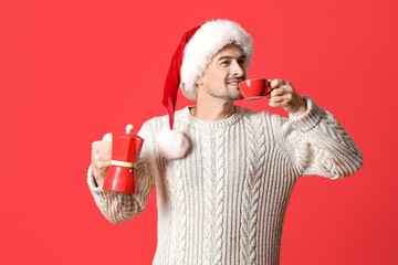 Handsome man in Santa with geyser coffee maker drinking espresso on red background