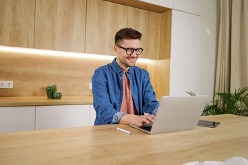 A contented man engages with a laptop in a wooden-clad workspace, accented with subtle greenery.