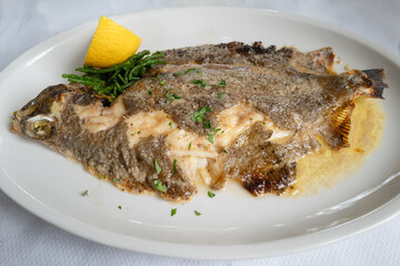 whole lemon sole fish cooked in butter on a white plate with a slice of lemon. - 786666478