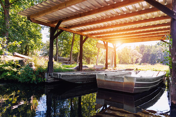 Old metal boat moored under shed shelter wooden canopy rustic boathouse at countryside in Spreewald canal national biosphere reserve house. Scenic Vintage water transport warm morning sunrise - obrazy, fototapety, plakaty