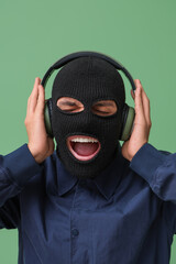 Handsome young happy man in balaclava with headphones on green background