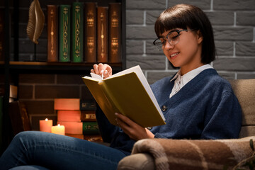 Young woman reading book in library at night