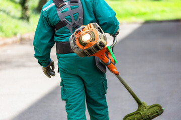 Worker in green uniform with a grass trimmer