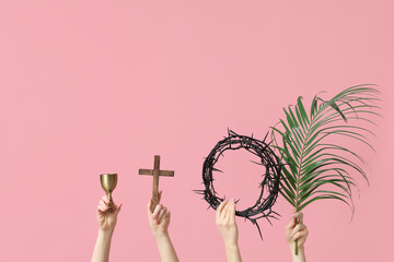 Female hands with wooden cross, crown of thorns and palm leaf on pink background. Good Friday...