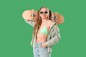Beautiful young woman in stylish outfit with skateboard on green background