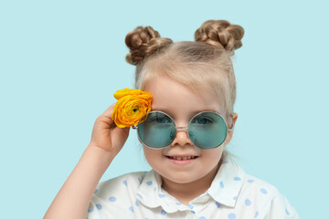 Cute little girl with beautiful yellow ranunculus flower on blue background