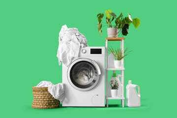 Modern washing machine with detergents and basket full of dirty clothes on green background