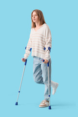 Injured young woman after accident with crutches on blue background