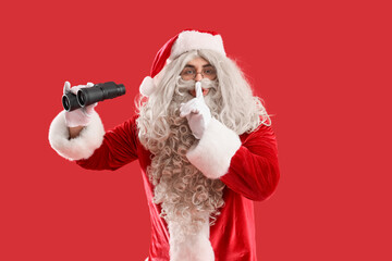 Santa Claus with binoculars showing silence gesture on red background