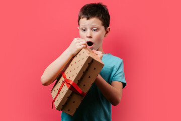 Surprised young boy holding a gift against pink background