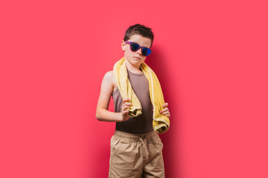 Confident boy with sunglasses and towel on pink background
