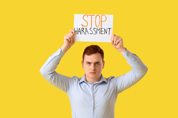 Young businessman holding paper with text STOP HARASSMENT on yellow background
