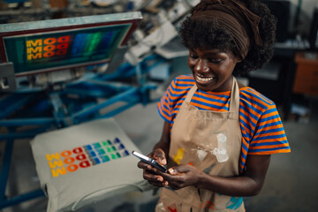 Happy interracial print shop employee using cellphone app at workshop.