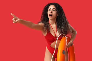 Beautiful young shocked African-American female lifeguard with ring buoy pointing at something on...