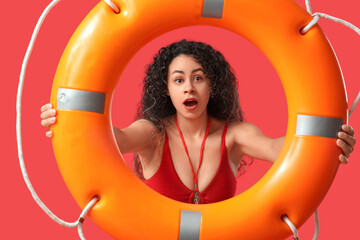 Beautiful young shocked African-American female lifeguard with ring buoy on red background - obrazy, fototapety, plakaty