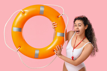 Beautiful young shocked African-American female lifeguard with ring buoy on pink background