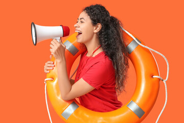 Beautiful young happy African-American female lifeguard with ring buoy and megaphone on orange...