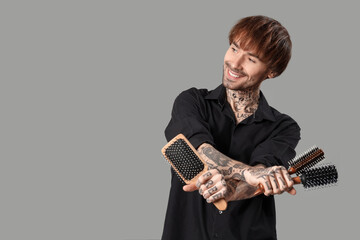 Fototapeta premium Young tattooed barber with hair brushes on grey background