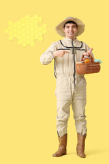 Male beekeeper pointing at basket of honey and paper honeycombs on yellow background