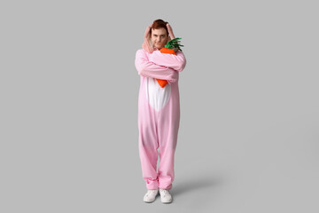 Thoughtful young man in Easter bunny costume holding plush carrot on white background