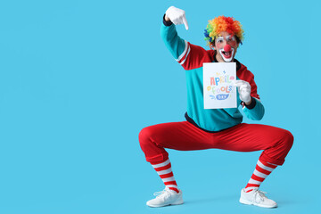 Portrait of clown pointing at poster with text APRIL FOOLS DAY on blue background