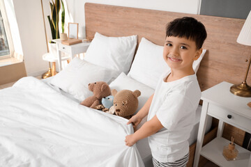 Cute happy little boy with toys making bed in bedroom