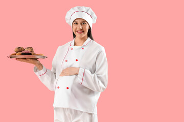 Young pregnant chef with pastries on pink background