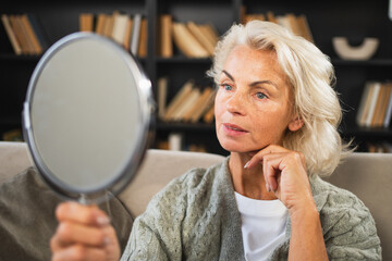 Love yourself. Beautiful old mature woman enjoying mirror reflection. Senior adult older lady looking at mirror confident happy on sofa at home. Woman doing daily morning beauty routine. Self love