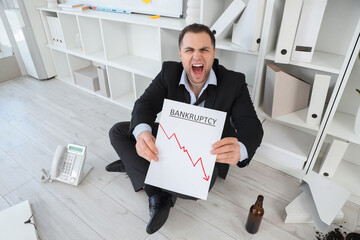 Drunk businessman holding paper with word BANKRUPTCY in office