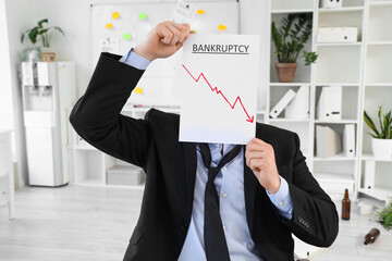 Young businessman holding paper with word BANKRUPTCY in office