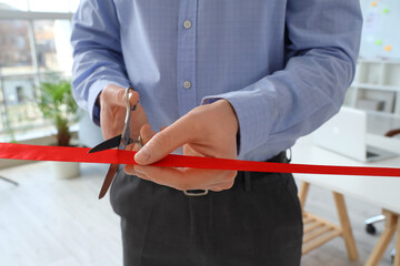 Businessman cutting red ribbon in office, closeup