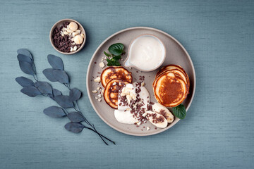 Traditional American Pancakes with banana honey cream, macadamia nuts and chocolate crumbles served as close-up on a Nordic design plate