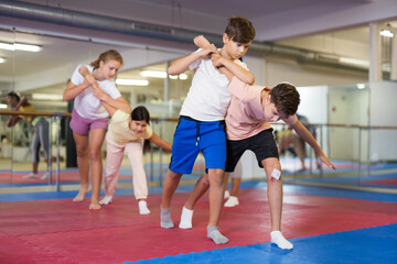 Fototapeta na wymiar Pair of teenage boys practicing self-defense moves during group training in gym