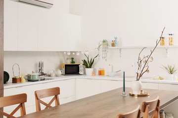 Vase with tree branches and Easter eggs on dining table in light kitchen