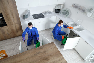 Male workers disinfecting drawers in kitchen