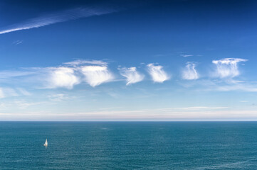 Série de cinq nuages aux formes originales dans un ciel bleu au-dessus d'un voilier sur la mer vus du site du Old Man of Stoer & Stoer Lighthouse en Ecosse
