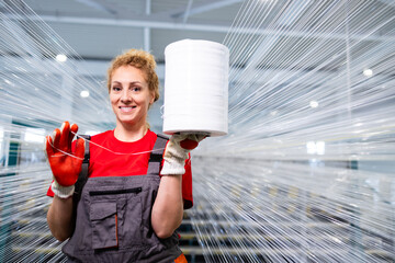 Beautiful female factory worker standing in textile factory and holding thread spool.