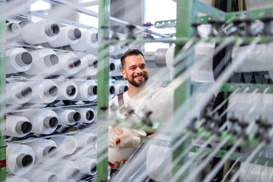 Experienced textile factory worker changing thread spool on industrial knitting machine.