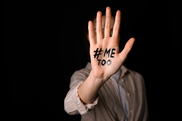 Woman with hashtag METOO on her palm against dark background, closeup